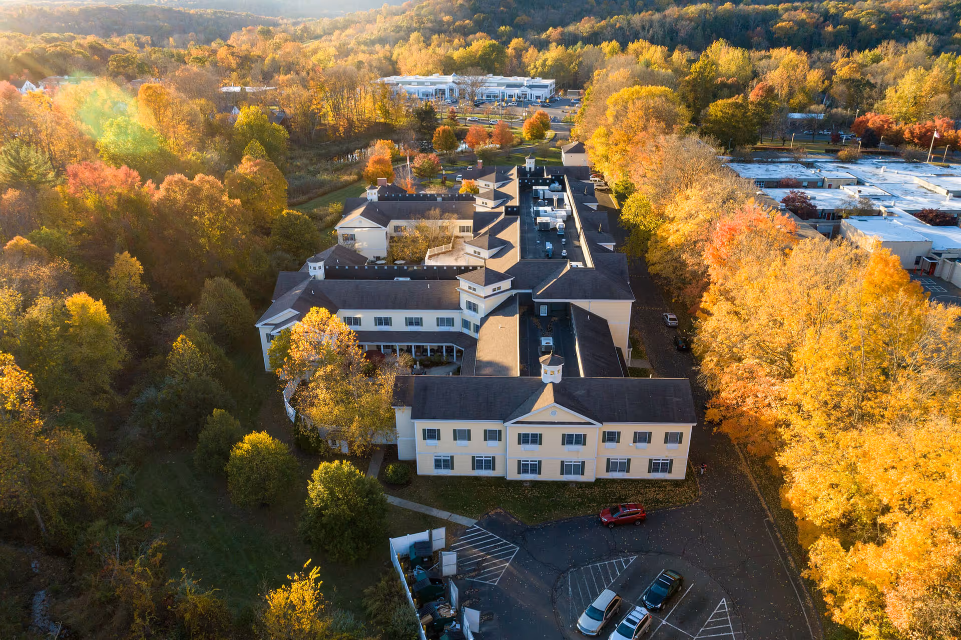 Aerial view of the Monarch Southbury senior living building nestled among trees with fall foliage and a parking lot.