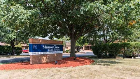 Exterior view of a senior living facility sign amid trees and landscaping.