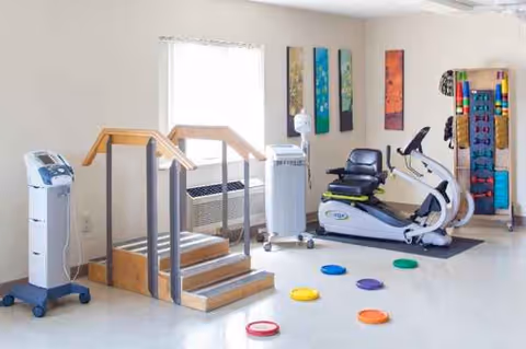 A bright senior living facility rehab gym with exercise equipment and mats.