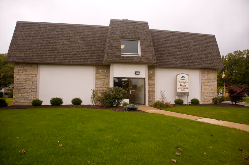 Front exterior of the Huntington Woods building showing the entrance, sign, and a green lawn.