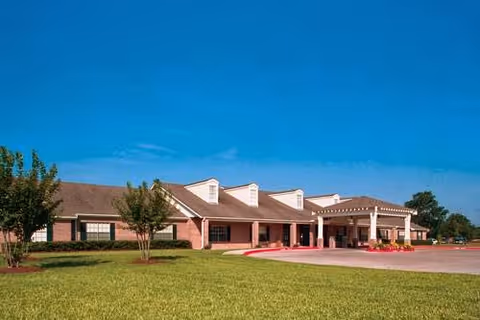 Exterior view of a single-story brick building with a covered entrance, surrounded by a well-maintained lawn and a few small trees under a clear blue sky.