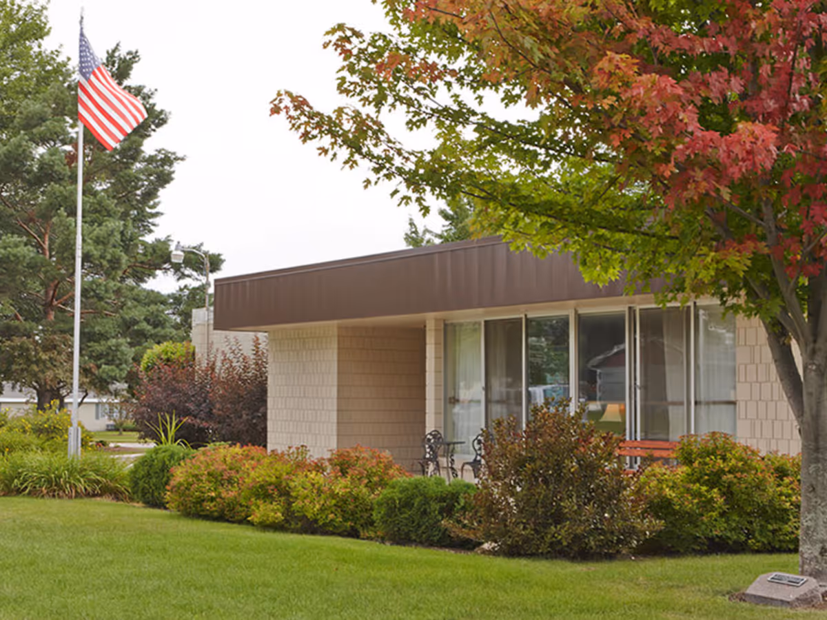 Exterior view of a senior living facility with landscaped gardens and a flag.