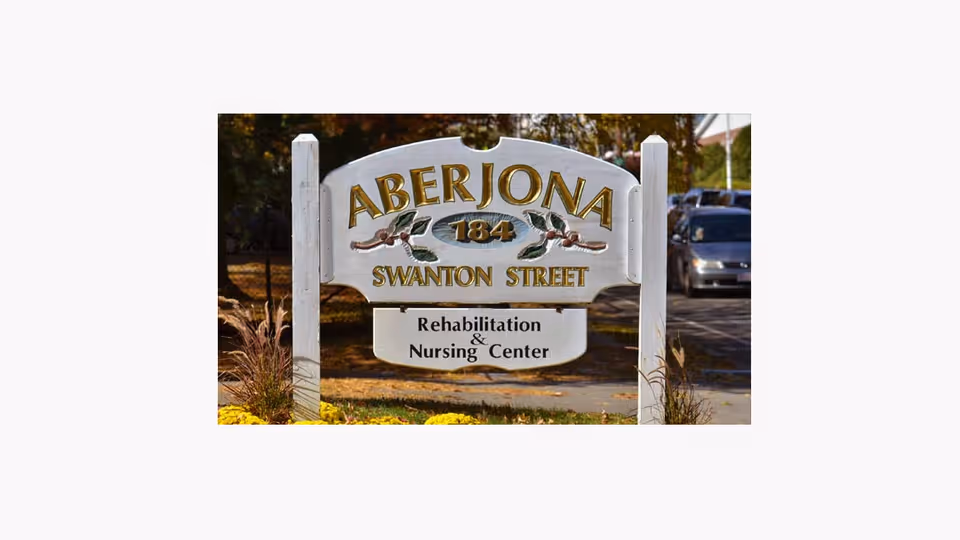 A wooden roadside sign reading "Aberjona 184 Swanton Street Rehabilitation & Nursing Center" at the facility entrance.