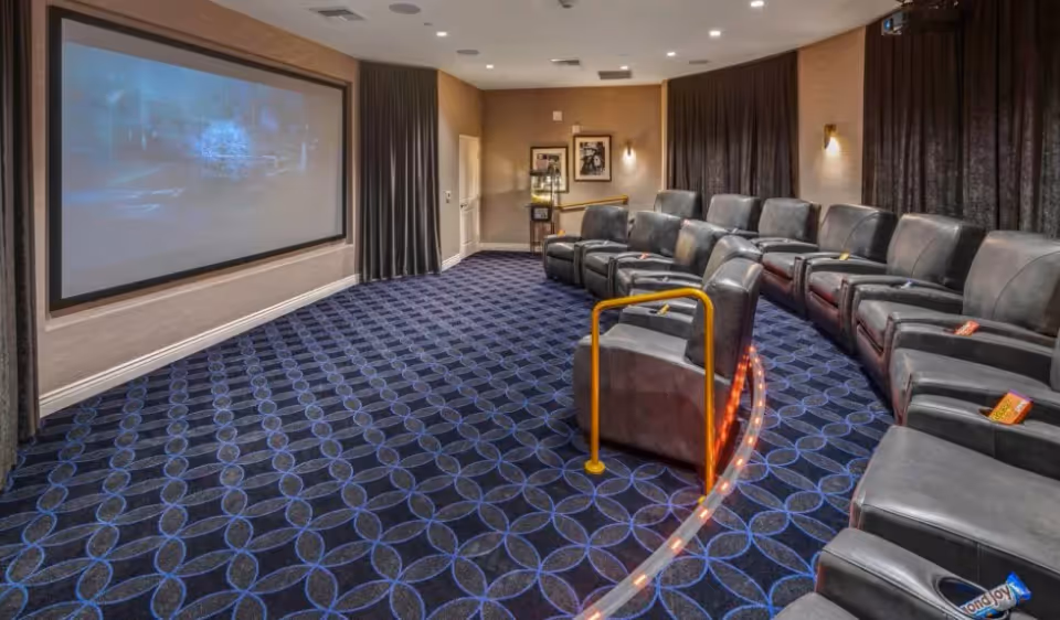 Small private movie theater with rows of reclining leather seats facing a large projection screen.