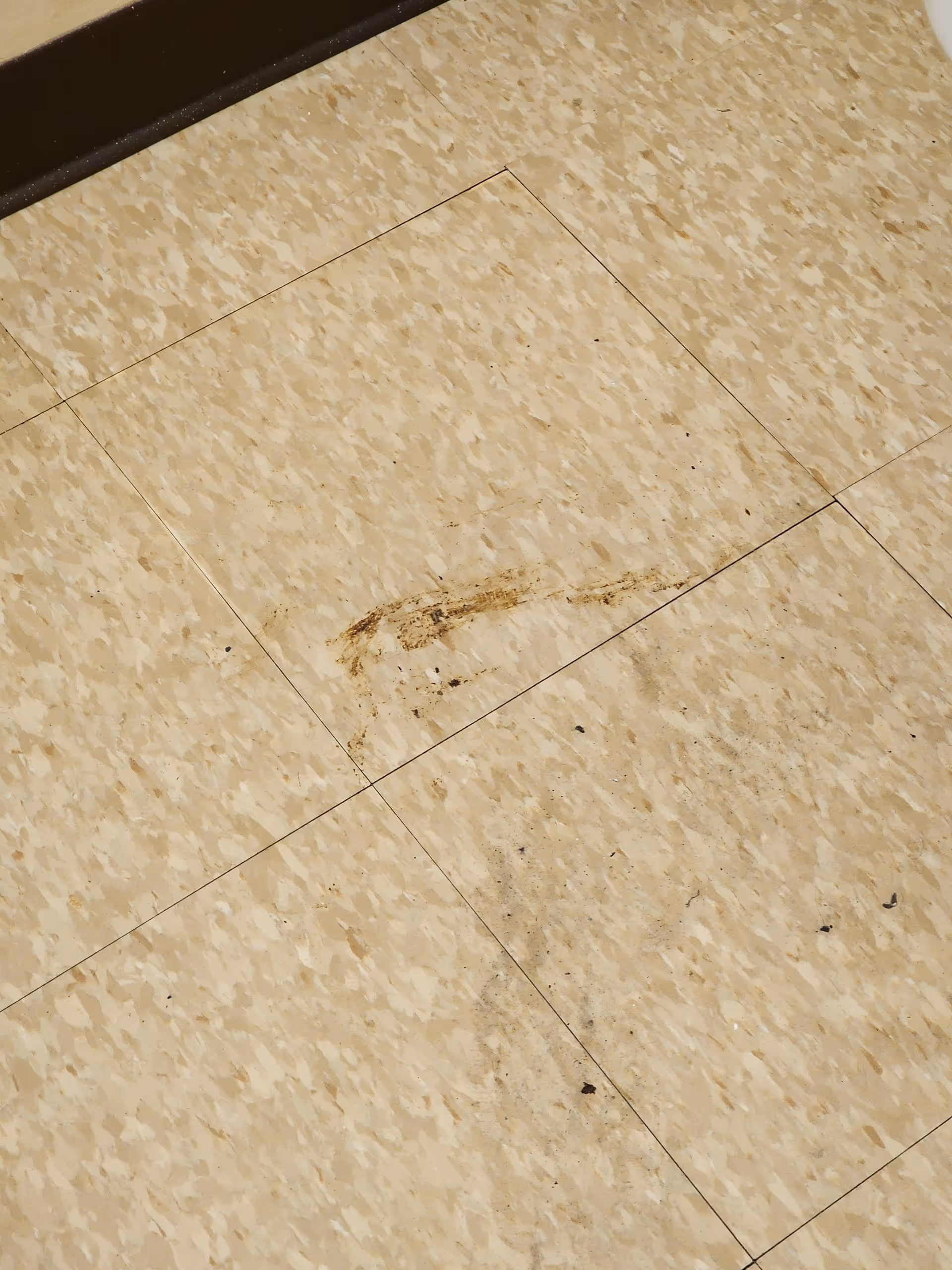 Close-up view of a beige tiled floor with visible dirt marks and scuffs on the surface.