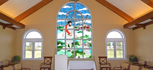 Interior chapel-style room with exposed wooden beams, a large stained-glass window depicting a biblical scene, a small altar/podium and seating.