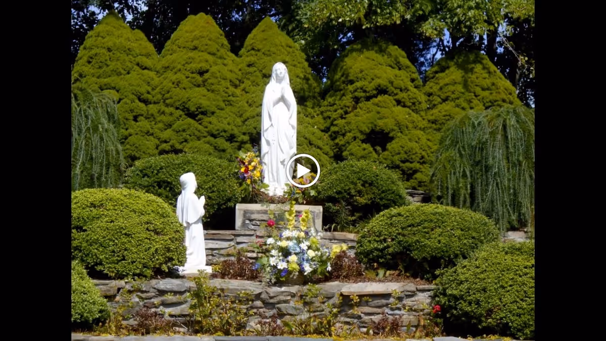 Stone terraced garden with two white religious statues surrounded by trimmed green bushes and flowers.