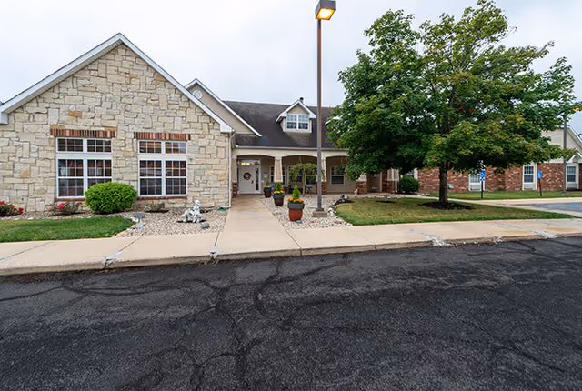 Front exterior of Kokomo Place senior living with stone facade, walkway, and trees