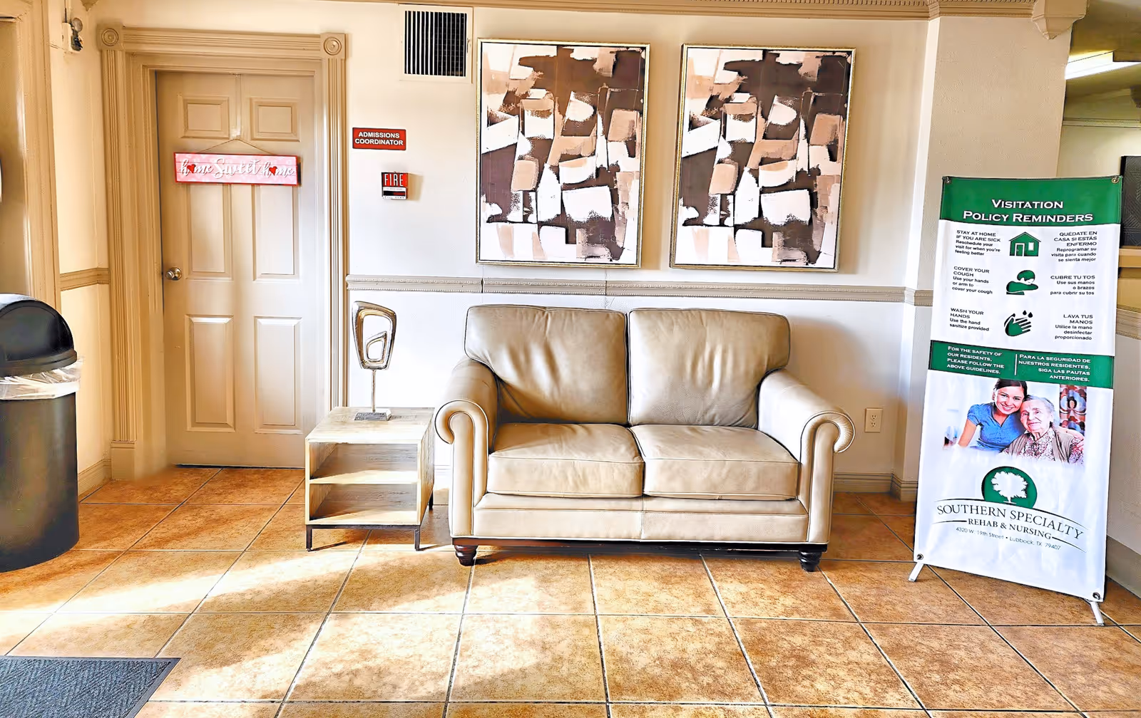 Lobby seating area with a beige leather loveseat, side table and a freestanding Southern Specialty Rehabilitation & Nursing banner.