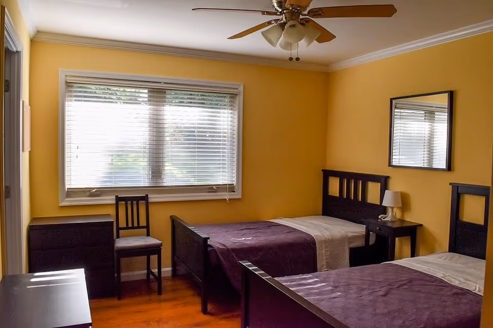 Two single beds with dark wood headboards in a yellow-walled bedroom.