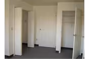 Empty bedroom with gray carpet and three white doors along one wall, two revealing closets.