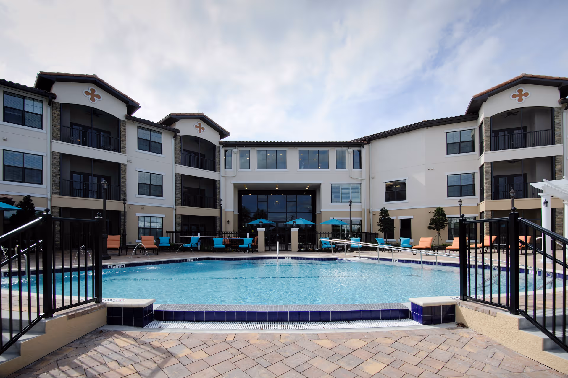 Outdoor swimming pool with lounge chairs and umbrellas in front of a three-story senior living building.