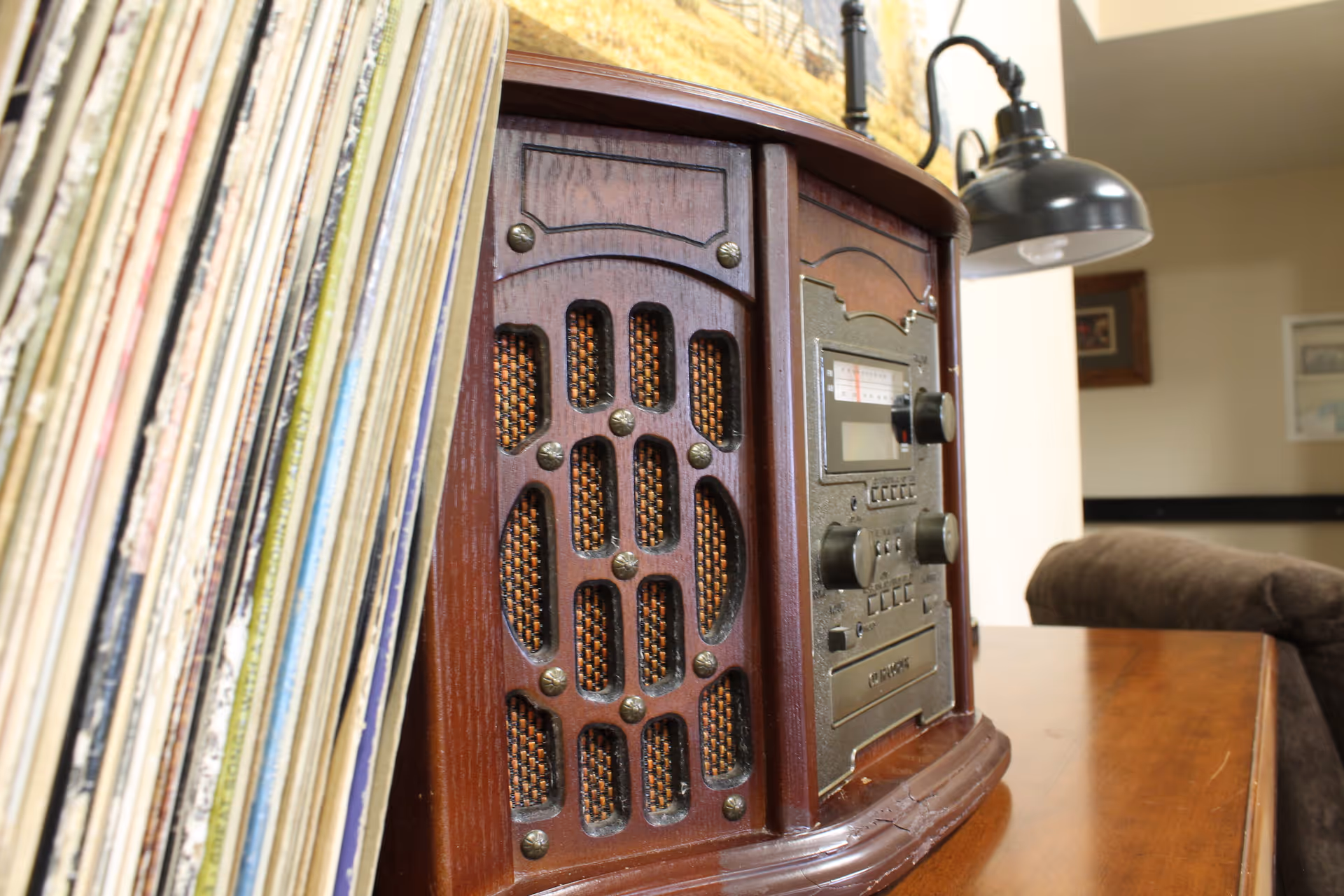 A vintage wooden tabletop radio with a stack of vinyl records on a wooden table in a living room setting.