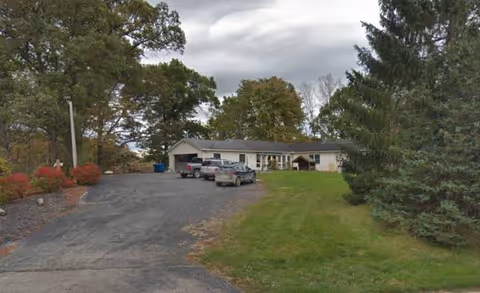 One-story facility with a curved driveway, several parked cars, and grassy landscaping.