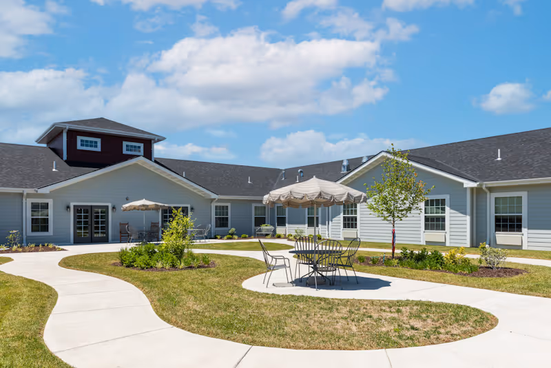 Courtyard outside a single-story building with paved winding walkways, patio tables and umbrellas on a sunny day.