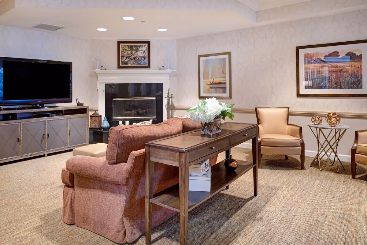 Cozy common living room with a sofa and console table, armchairs, a wall-mounted TV, and a fireplace.