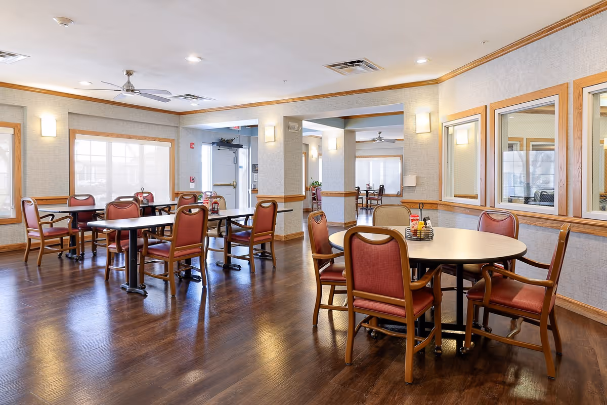 Bright, spacious dining area with round and rectangular tables and red upholstered chairs on dark wood floors.