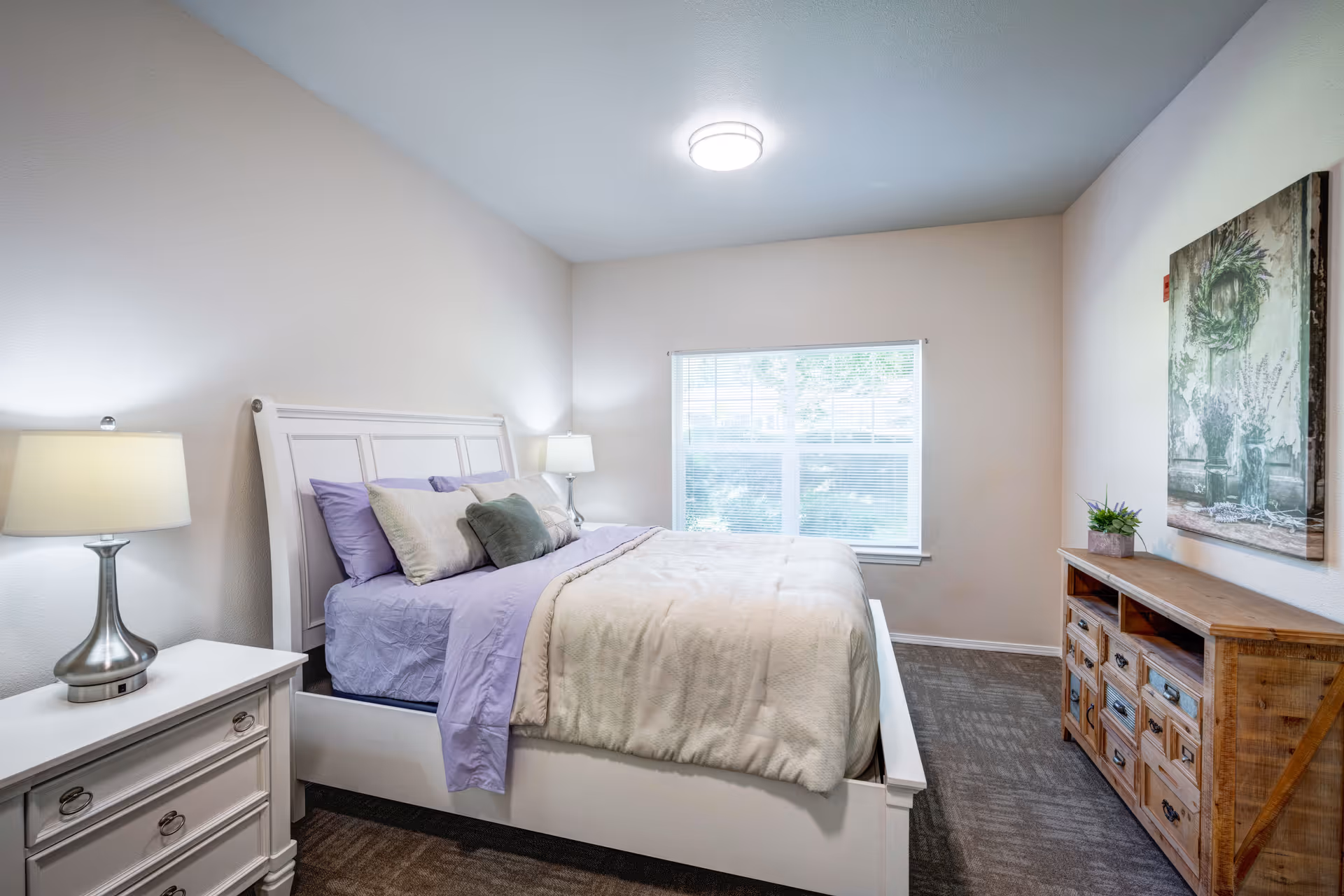 Bright, neatly arranged bedroom with a white bed dressed in light linens, two bedside lamps, a wooden dresser, and a window.