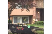 Ground-level brick apartment facade with a large window, landscaped mulch beds and decorative pinwheels.