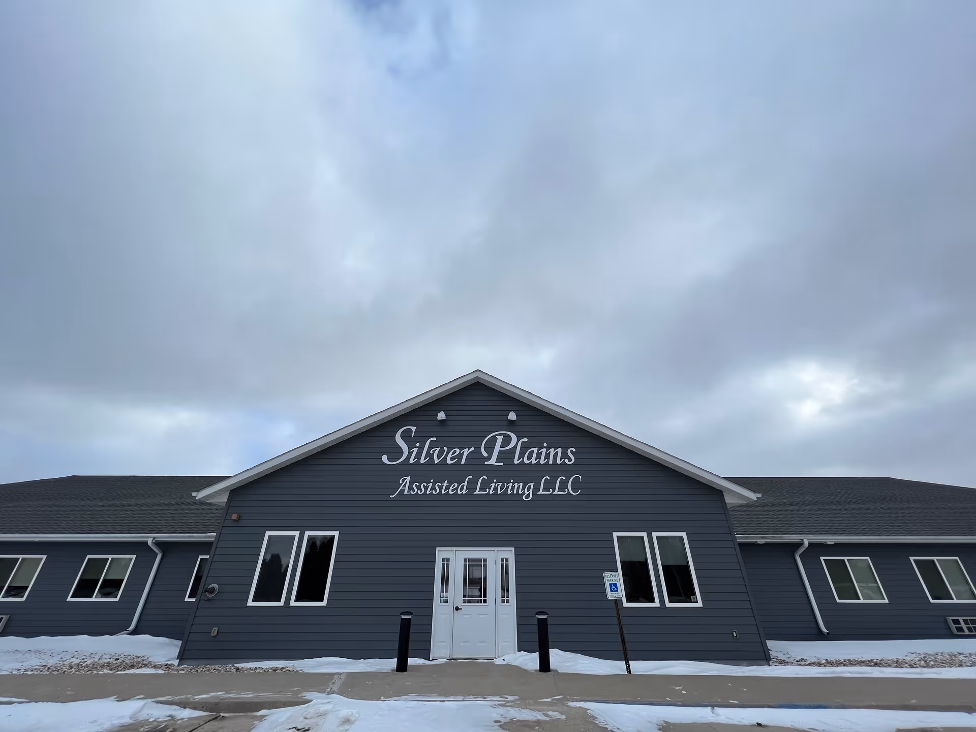Front exterior view of Silver Plains Assisted Living LLC building on a cloudy day with snow on the ground and a sidewalk leading to the entrance.