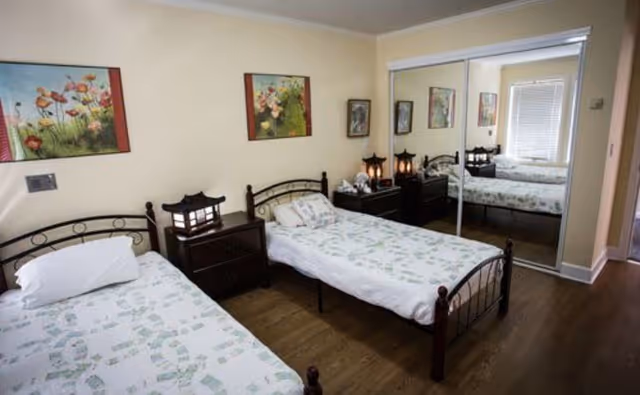 Two twin beds with floral bedding in a bright bedroom featuring nightstands, decorative lamps, wall art, and mirrored closet doors.