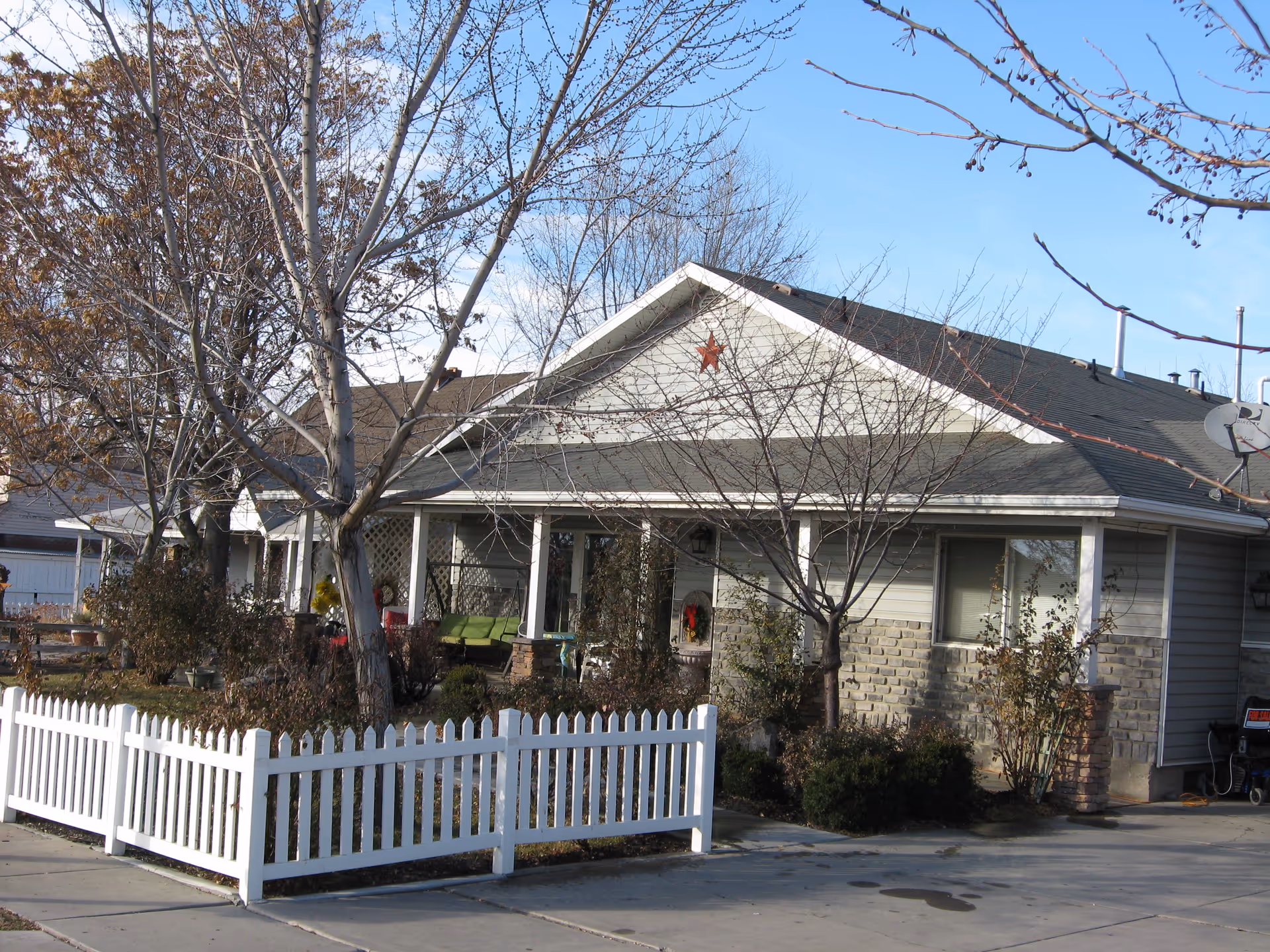 Sunny exterior view of a single-story senior living villa with a white picket fence.