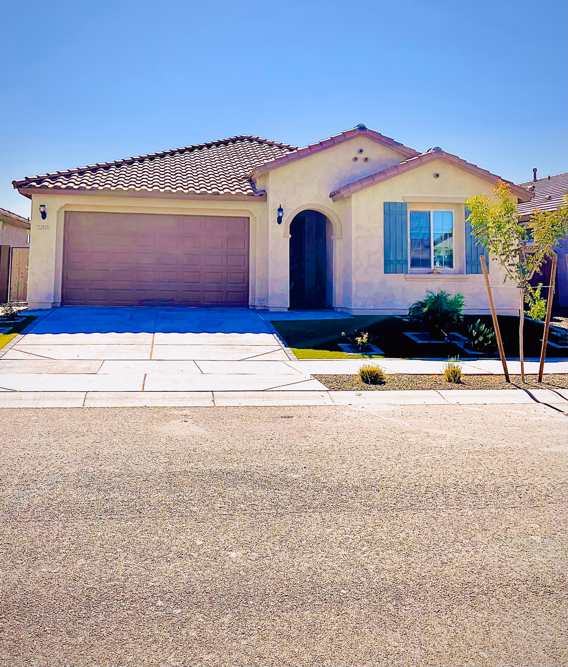 Front exterior of a single-story stucco house with a two-car garage, arched entryway, blue shutters, and a driveway.