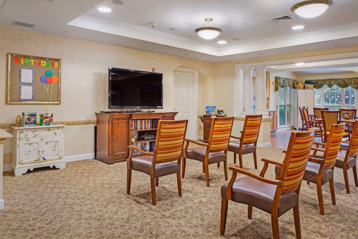 Community activity room with rows of wooden chairs facing a large TV and cabinet.