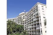 Exterior view of a multi-story retirement residence building with balconies on each floor, set against a clear blue sky and surrounded by green trees.