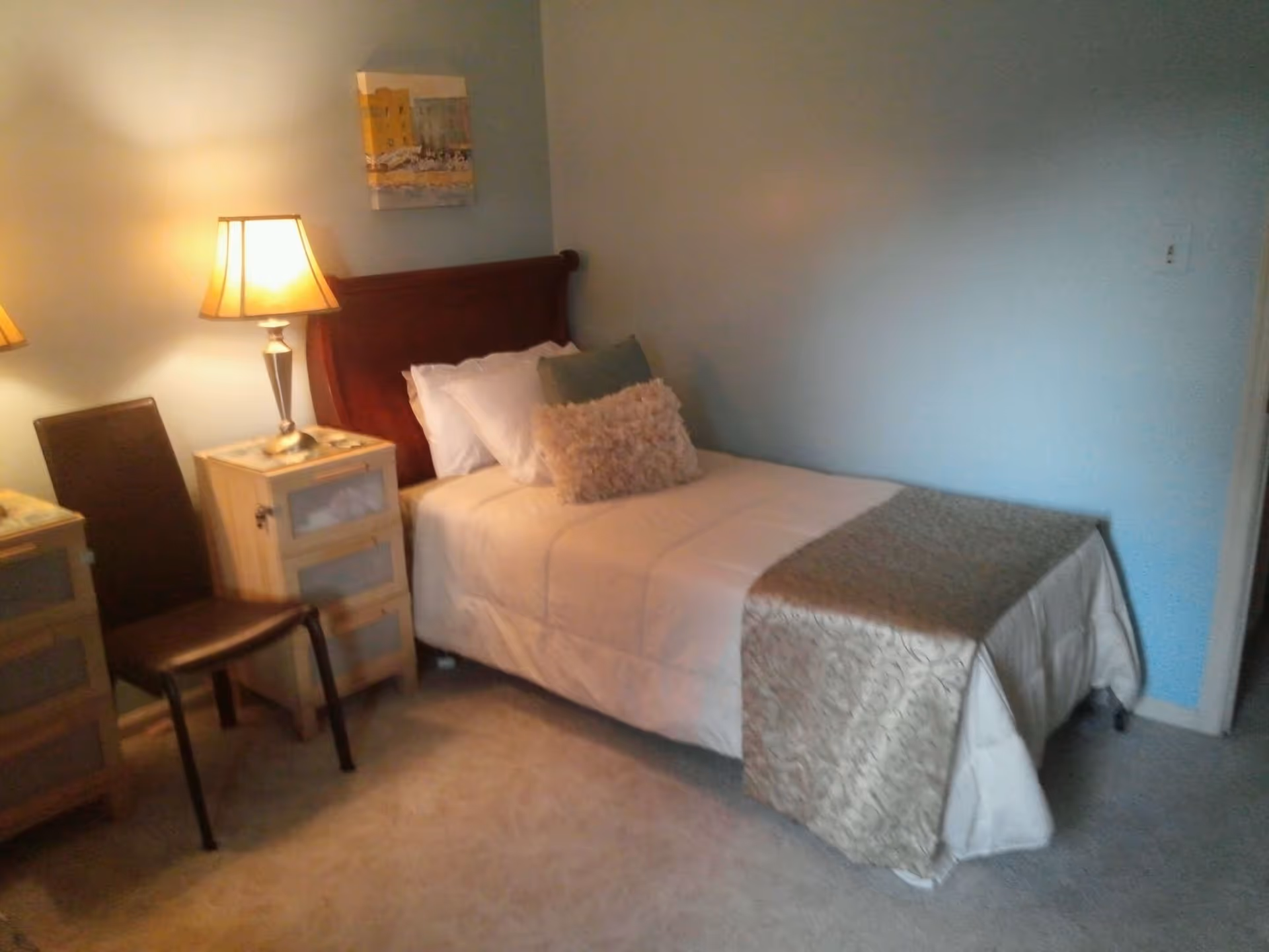 Single-occupancy bedroom with a twin bed, bedside tables with lamps and a chair against a light blue wall.