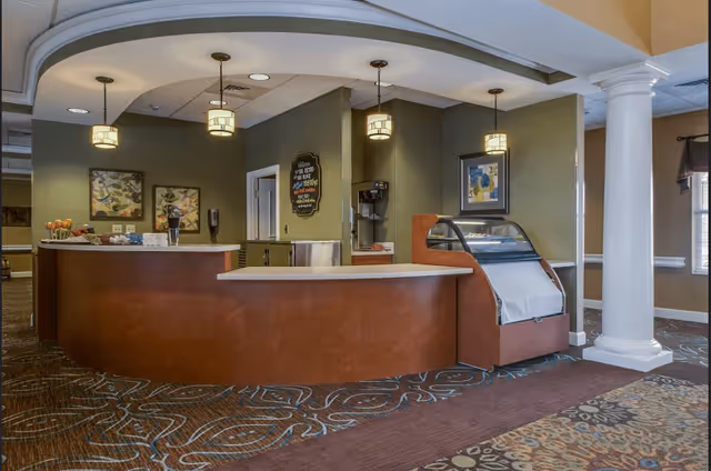 Reception area with a curved wooden desk, three hanging pendant lights, a decorative carpet, framed artwork on the walls, a white column, and a small display case on the right side.