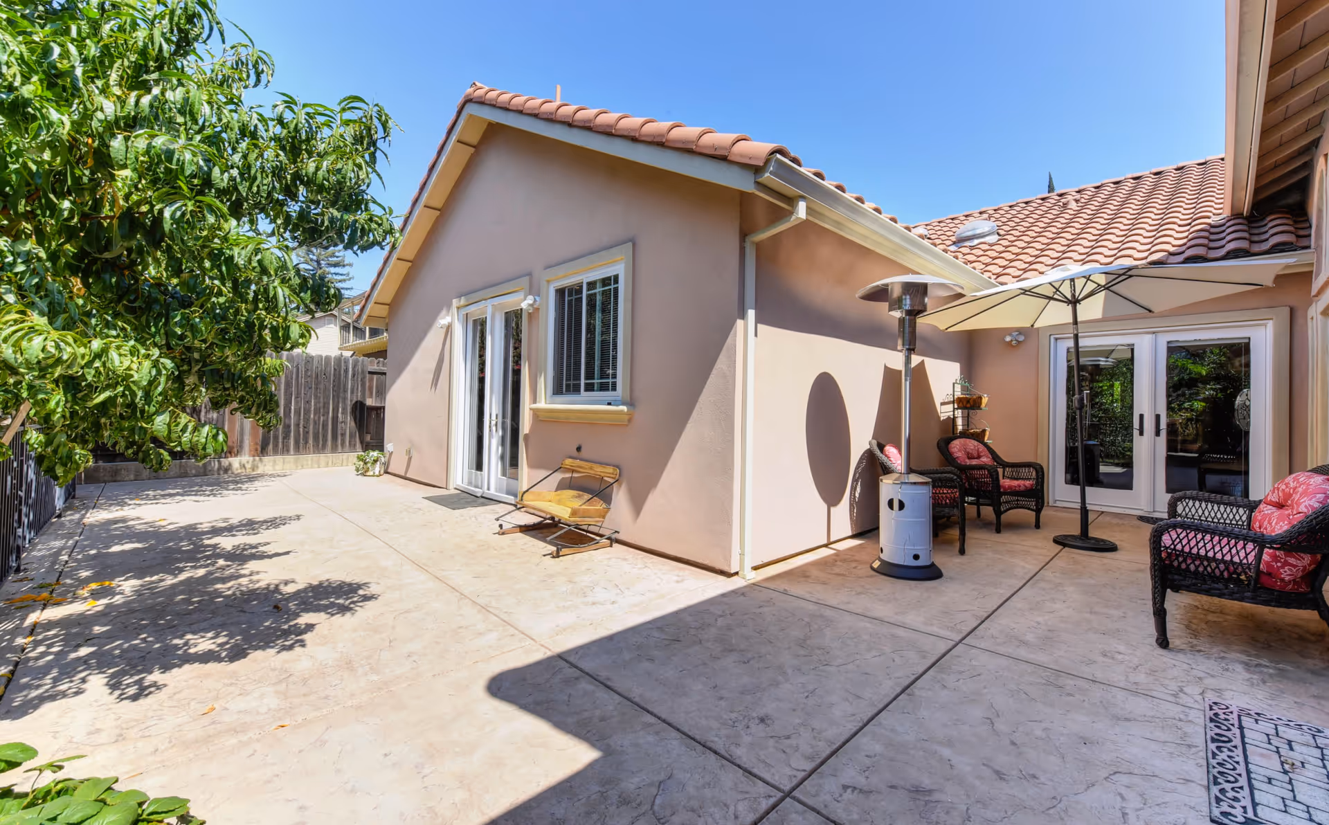 Sunny enclosed patio with a tiled-roof house, outdoor seating, umbrella and a patio heater.