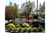 Outdoor view of a healthcare center sign labeled Southridge Health Care Center surrounded by green bushes and trees, with a building and parked cars in the background.