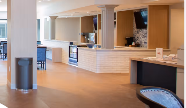 Bright open common area with a white-tiled service counter, seating, columns, and a reception desk.