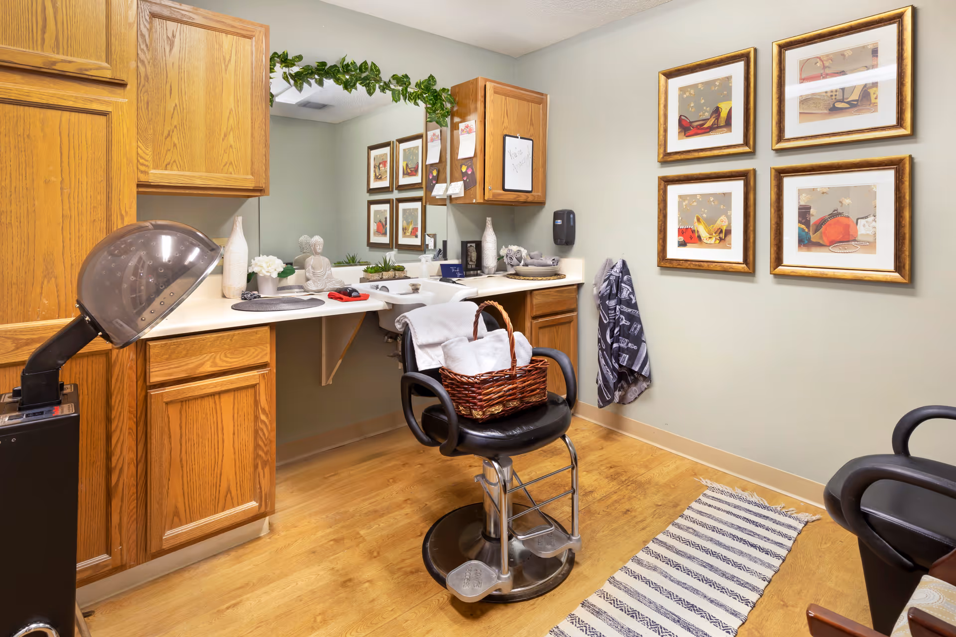 Small salon-style room with a styling chair under a hooded hair dryer, countertop with mirror and oak cabinets.