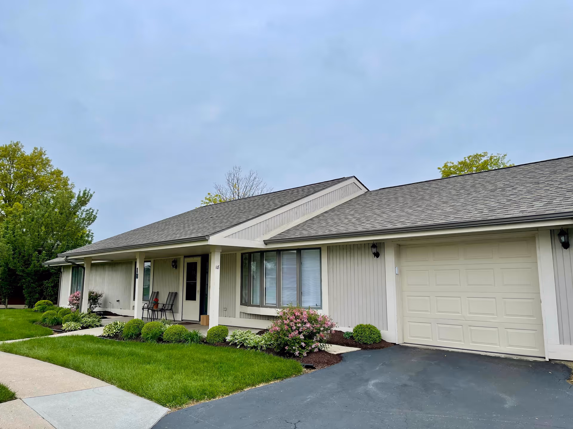 Single-story ranch-style residence with a front porch, attached garage, and landscaped lawn under an overcast sky.