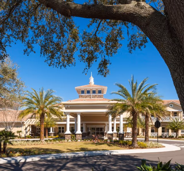 Sunlit exterior view of HarborChase of Villages Crossing with palm trees and columns.