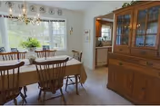 Sunlit dining room with a wooden table and chairs, a chandelier, and a large china cabinet by a window.