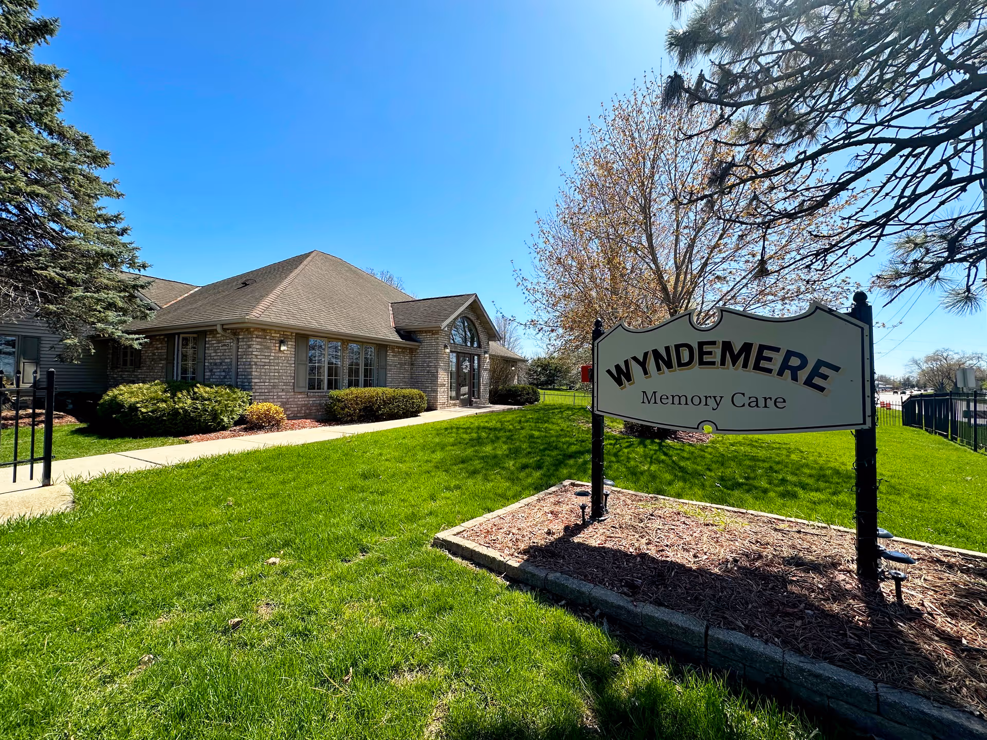 Front exterior of the Wyndemere Memory Care building with a lawn and entrance sign.