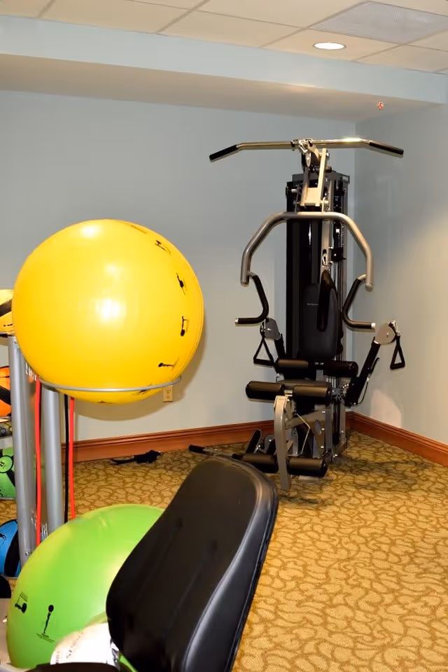 Small exercise room with a multi-station weight machine, colorful stability balls, and a workout bench.
