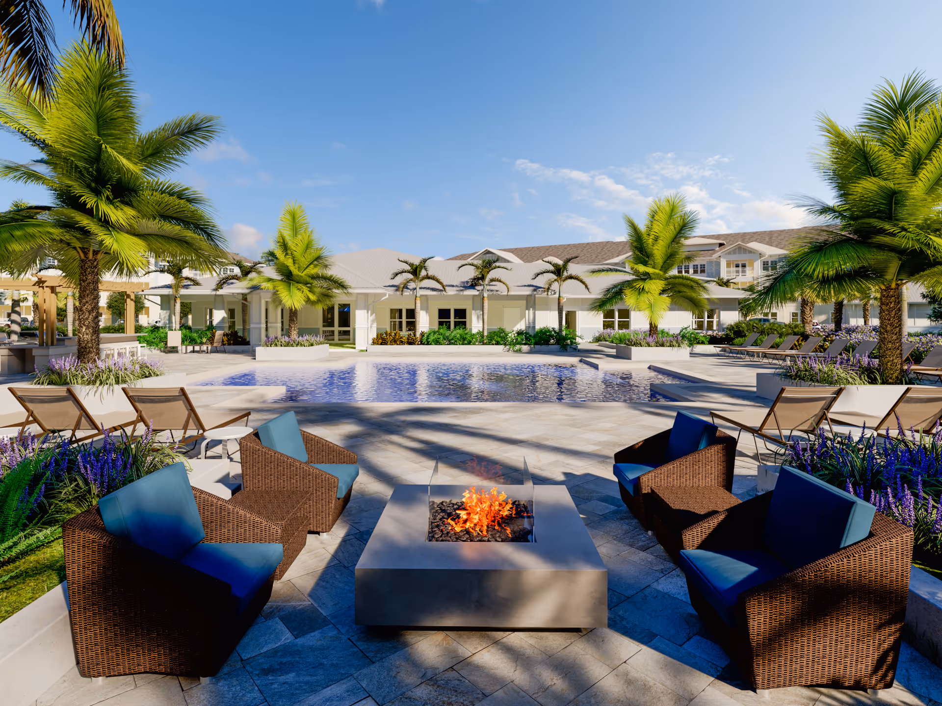 Outdoor patio area at The Sovana At Stuart featuring a modern fire pit surrounded by four wicker chairs with blue cushions, a swimming pool in the background, palm trees, lounge chairs, and a clear blue sky.