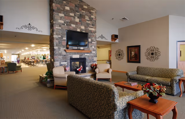 Comfortable communal lounge with sofas, armchairs, a stone fireplace and wall-mounted TV opening into a dining area.