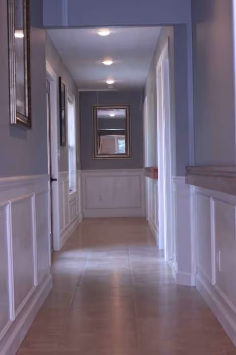Narrow, well-lit hallway in Briar Hill Assisted Living with wainscoting and mirrors.