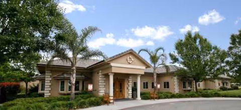 Riverwalk senior living facility exterior with arches, columns, palm trees, and manicured landscaping.