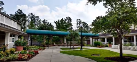 Outdoor courtyard at Brookdale Willowbrook Place with walkway, green awnings, and landscaped plants.