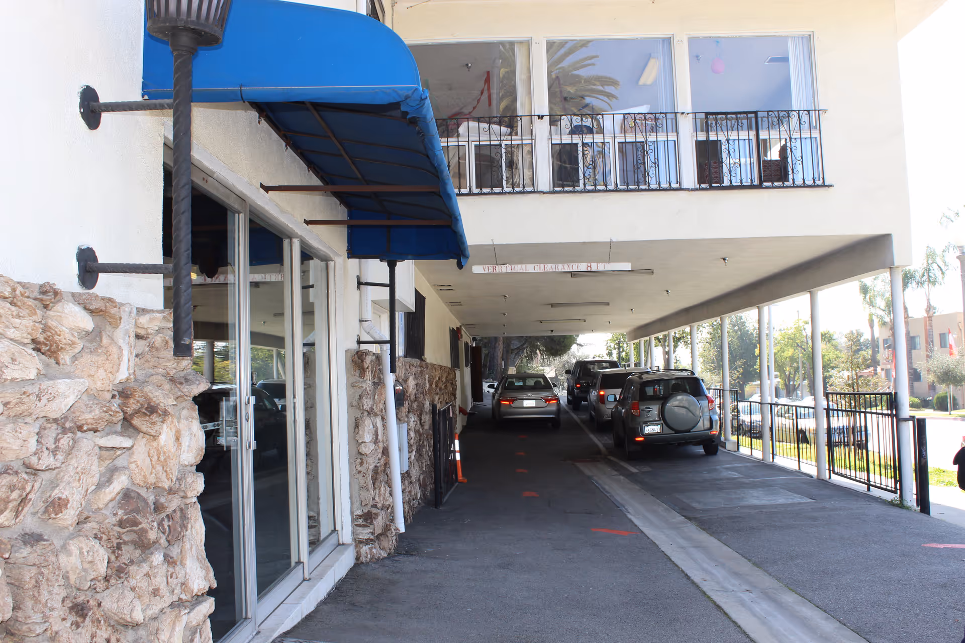 Covered drive-through entrance of a building with parked cars under a blue awning and stone-clad wall.