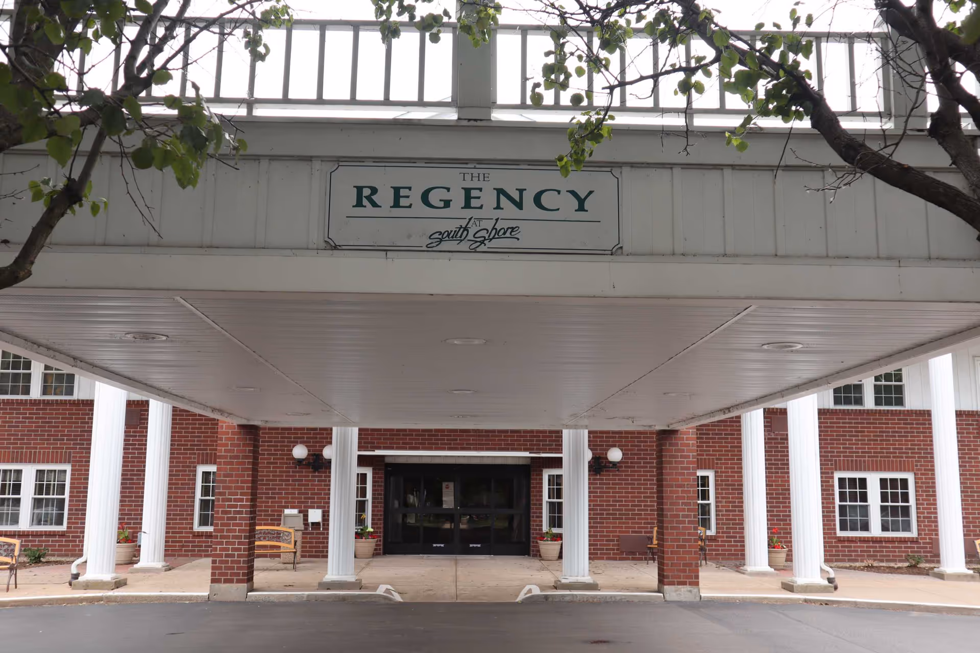 Covered entrance canopy of The Regency at South Shore with white columns and a red brick facade and sign above the drive.