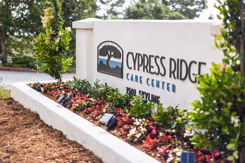 Entrance sign reading "Cypress Ridge Care Center" set in a low stone planter with flowers and landscaping.