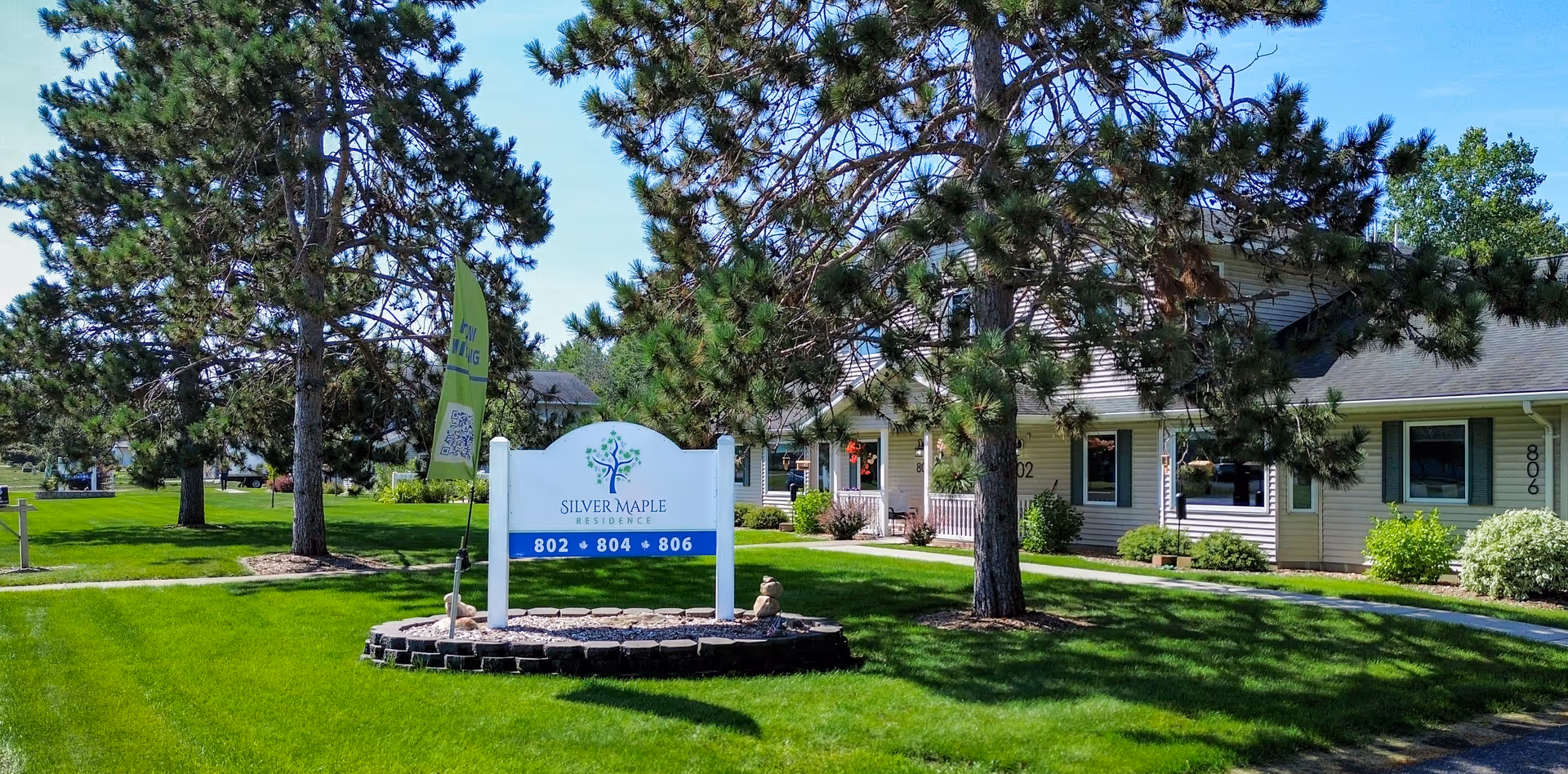 Sign reading 'Silver Maple Residence' on a manicured lawn with trees and the facility's single-story building in the background.