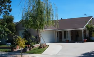 Single-story suburban home with an attached garage, front porch, driveway, and landscaping including a small weeping tree.